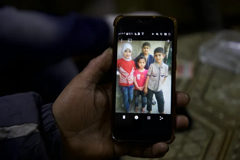 eastern-ghouta-tawfiq-daem-holds-up-a-photo-of-his-four-children-who-were-kiled-1734533758.webp